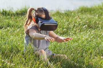 Fototapeta premium Little girl plays game with virtual reality glasses outdoors