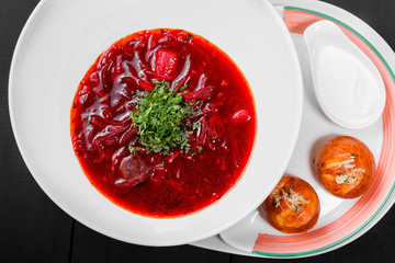 Ukrainian and Russian traditional beetroot soup - borscht in plate, sour cream and buns with garlic and herbs on dark wooden background. Homemade food