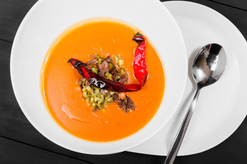 Tomato soup, red pepper soup, sauce with olive oil, meat and pickles in bowl on black wooden background, healthy food. Top view