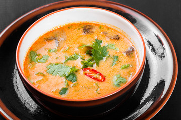 Soup with meat in bowl with oregano, peppers and vegetables on dark wooden background. Homemade food