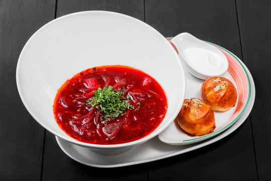 Ukrainian and Russian traditional beetroot soup - borscht in plate, sour cream and buns with garlic and herbs on dark wooden background. Homemade food