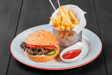 Burger, hamburger with french fries, ketchup, mayonnaise, fresh vegetables and cheese on plate on dark wooden background. American fast food. Top view