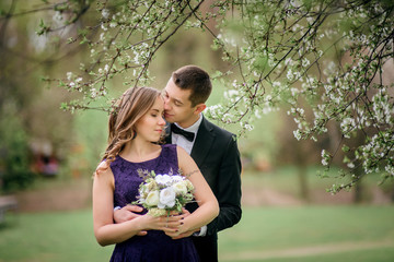 Young couple with wedding bouquet stands under the tree
