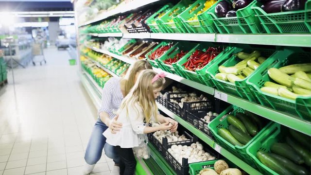 A woman with a young girl chooses mushrooms on the shelves of the supermarket