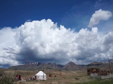 Clouds flying in a deep blue sky with ethnic yurts and mountains in background