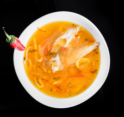 Soup chicken - broth with noodles, herbs, pepper and vegetables in bowl, isolated on black background, healthy food. Top view