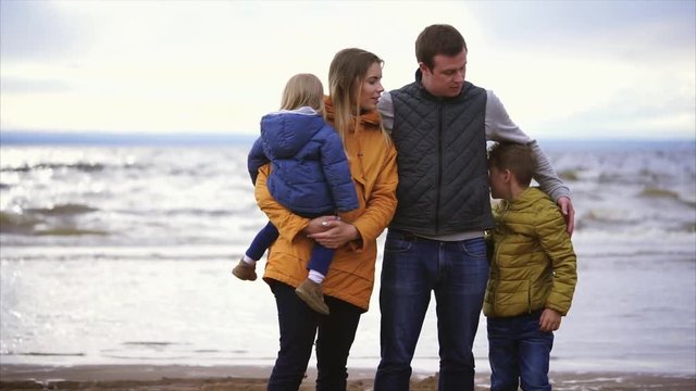 The adult spouse and his wife are standing with a small child in their arms and grown up by an adult son near the sea and enjoying a day off, this is a friendly and joyful family