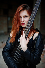 Red haired punk girl wear on black with bass guitar at abadoned place. Portrait of gothic woman...