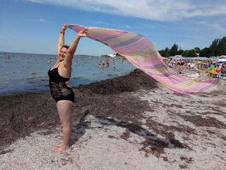 A woman is holding a developing pareo in the wind standing on a beach