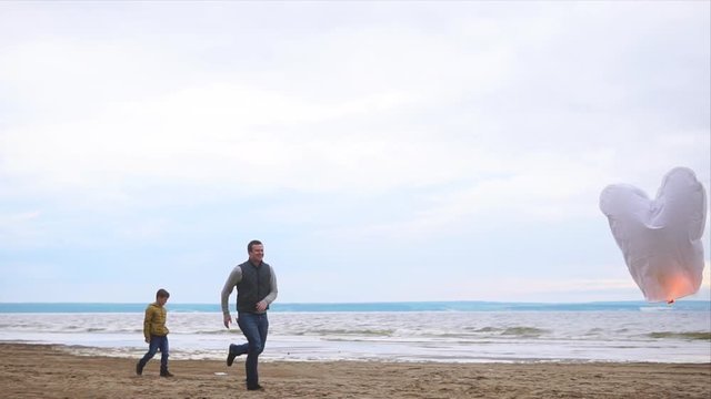 A young family who spends the weekend on the beach near the sea looking at the flashing paper flashlight, Dad runs after the flashlight to direct the flow of air