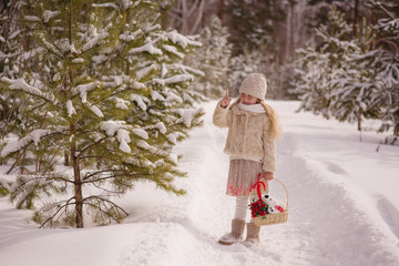 little cheerful girl holding, shaking a basket with a gift in a winter forest