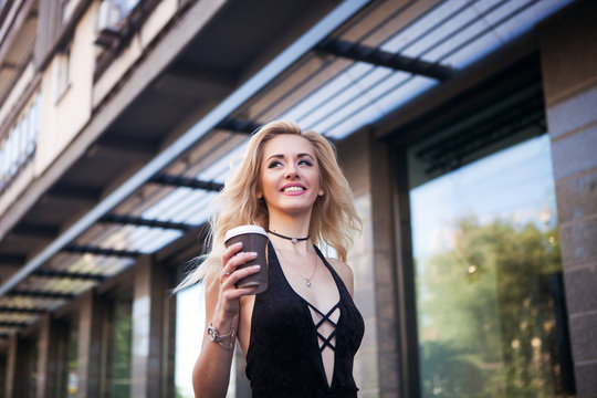 Close up portrait of happy laughing woman in a casual outfit walks in the city . Beautiful sexy blonde keeps coffee and laughing