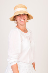 portrait of a attractive blond haired mid aged european woman wearing white dress and a beige summer head showin happy face - half body - studio shot on white background.