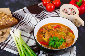 Stew with meat and vegetables in tomato sauce on dark background