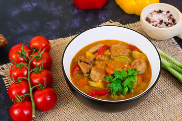 Stew with meat and vegetables in tomato sauce on dark background