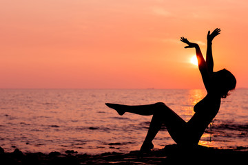 Woman silhouette sitting on sunset sea background, side view, back lit