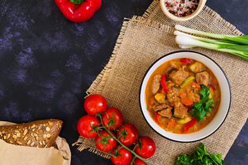 Stew with meat and vegetables in tomato sauce on dark background
