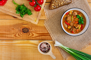 Stew with meat and vegetables in tomato sauce on wooden background. Top view