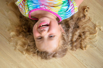 Happy little girl with blond curly hair upside down.