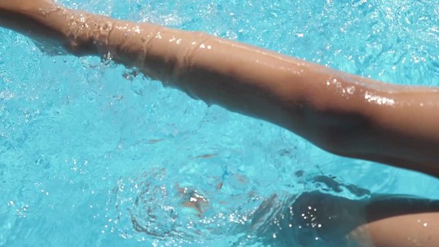 Girl sitting on the edge of a pool dangling feet in the water. Slow motion.