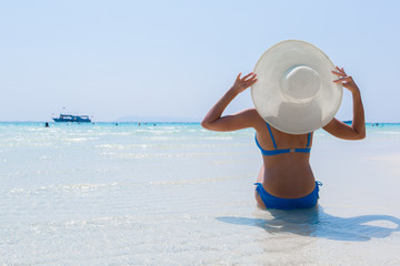 Woman in white hat sitting on the seashore in water, blue sea background