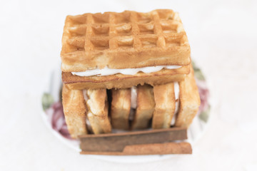 Viennese waffles with cream filling and one stick of cinnamon lie on a white saucer with a floral pattern in the defocus on a white background