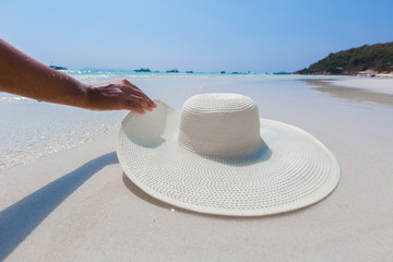 Female hand holding white hat on the beach