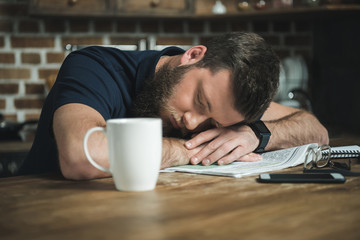 Obraz premium portrait of tired man sleeping on table with newspaper and coffee cup