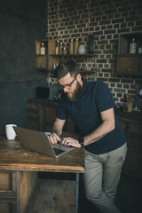 young casual caucasian man working on laptop while standing in the kitchen