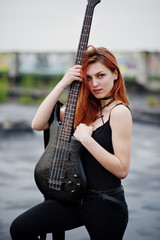 Red haired punk girl wear on black with bass guitar at the roof.