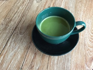 closeup green tea in green ceramic cup was put on wooden desk,in vintage warm light tone,blurry light around.