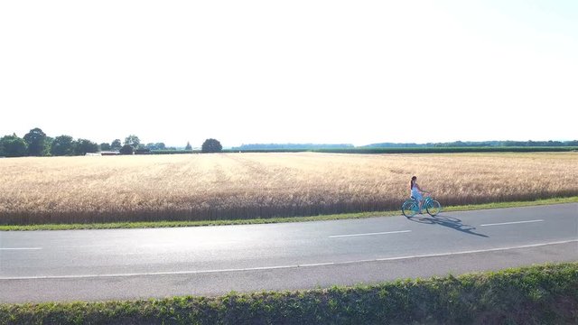 Flying beside female person bicycling at wheat field 4K