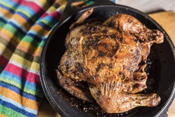 Fried fat chicken lays in a black frying pan on a multicolored striped background