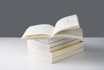 Pile of books with one book open on white table.