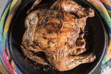 Grilled chicken lays in a black frying pan on a background of a colorful striped towel, close-up