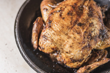 Baked chicken lays in a black frying pan on the right side of the frame on a light blurred background