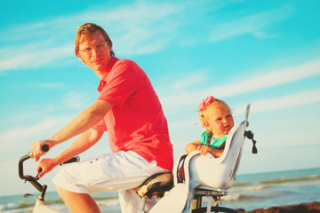 father and little daughter biking on beach