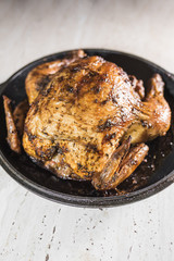 Fried chicken is in a black frying pan on a light beige with dark interspersed background