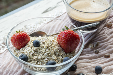 Bowl with cereals and berries and cup of coffee on the pink tissue in the daylight