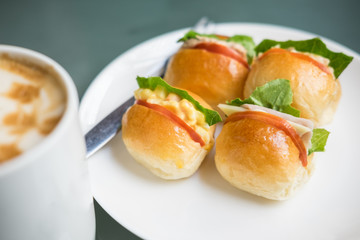 Mini tuna, ham cheese , corn burgers, party food on white plate and fork served with hot latte coffee mug - selective focus