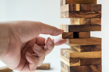 Close up of man's hand take one block from the tower stack from wooden blocks toy isolated on white background