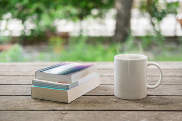 White mug of hot coffee and books on wooden table