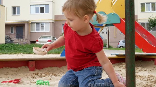 The Girl Is Playing In The Sandbox. A Preschool Child Is Playing In The Sand, An Urban Landscape.