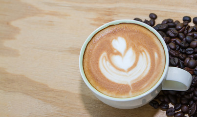 A cup of coffee with heart pattern in a white cup on wooden background