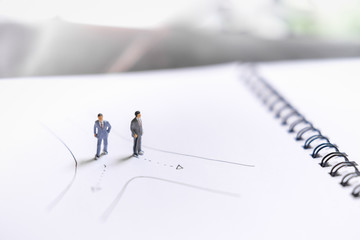 Two miniature figures business man standing on notebook with drawing line - business concept