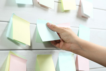 womans hand sticking notepapers on white wooden board