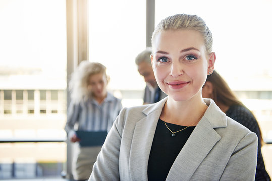 Confident young businesswoman smiling with coworkers talking in the background