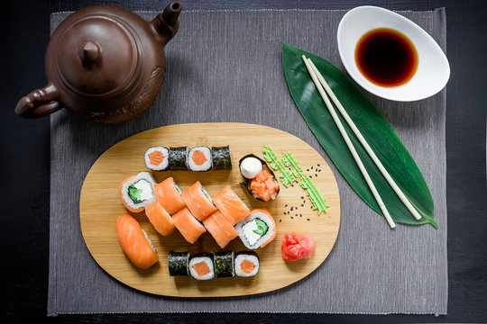 Japanese sushi rolls, soy sauce, ginger and chopsticks on dark background. Top view. Flat lay.