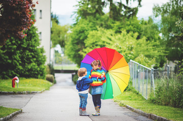 Two adorable kids playing outdoors with big colorful umbrella