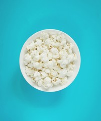 White fluffy movie theater popcorn in a bowl on blue background, top view. Cinema concept with classical popcorn
